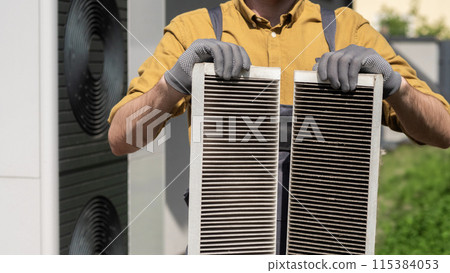 Man with gloves holding two clogged air filters from a home ventilation system. 115384053