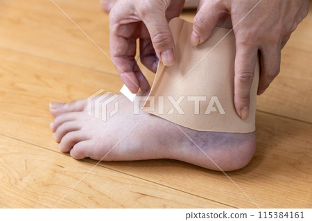 一位女士正在對扭傷的腳踝進行敷料 一位女士正在對扭傷的腳踝進行敷料 115384161