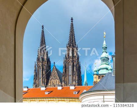 The twin spires of St. Vitus Cathedral rise majestically above Prague Castle, framed by an archway under a cloudy sky. Prague, Czechia The twin spires of St. Vitus Cathedral rise majestically above Prague Castle, framed by an archway under a cloudy sky. Prague, Czechia 115384328