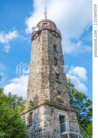 Rising against a blue sky, the stone lookout tower on Prosecsky Hreben in the Jizera Mountains stands as a point of interest for visitors seeking panoramic views. 115384359