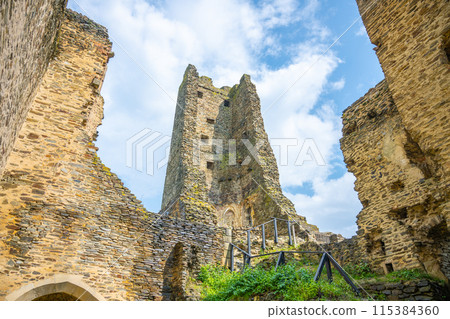 The ancient walls of Okor Castle stand tall against a clear blue sky, with remnants of fortifications and archways hinting at past grandeur. Czechia 115384360