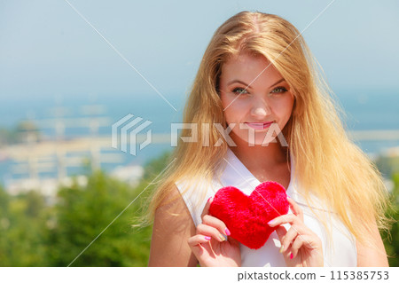 Happy blonde girl holding heart shape pillow 115385753