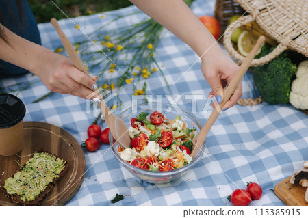 Woman mixes vegan salad on picnic outside. Vegan food concept Woman mixes vegan salad on picnic outside. Vegan food concept 115385915