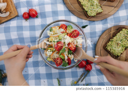 First person view of woman mixes vegan salad on picnic outside. Vegan food concept 115385916
