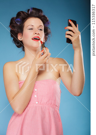 Girl in hair curlers applying red lipstick 115386317