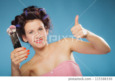 woman in hair rollers holds makeup brushes 115386330