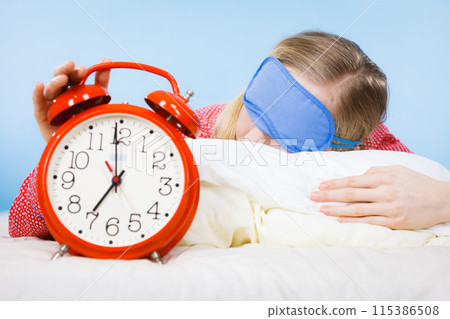 Sleeping woman wearing pajamas holding clock 115386508