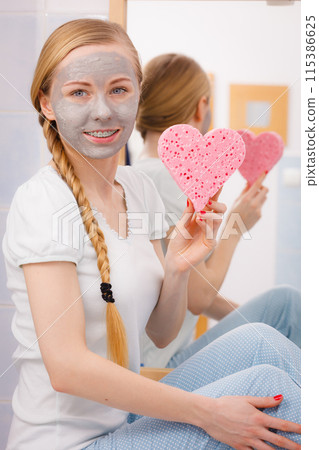 Woman having grey face mask holding heart sponge 115386625