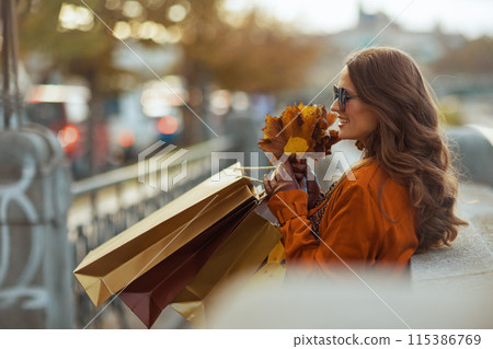 happy stylish female in orange trench coat with shopping bags 115386769