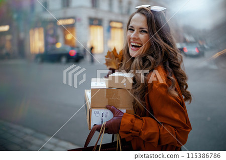 smiling stylish woman in brown trench coat with parcels smiling stylish woman in brown trench coat with parcels 115386786