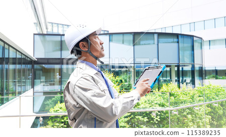 Engineer checking a building while looking at a tablet Engineer checking a building while looking at a tablet 115389235