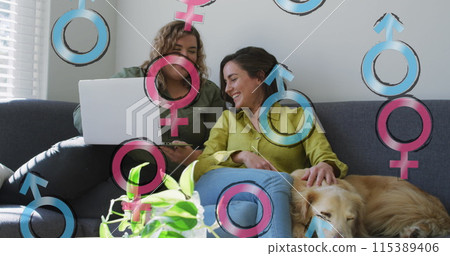 Image of male and female symbols over lesbian couple using laptop 115389406
