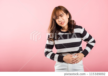 Portrait of Asian beautiful young woman has stomachache, female abdominal pain suffering from stomach ache, studio shot isolated on pink background, period pain, Health and medical gastritis concept Portrait of Asian beautiful young woman has stomachache, female abdominal pain suffering from stomach ache, studio shot isolated on pink background, period pain, Health and medical gastritis concept 115389892