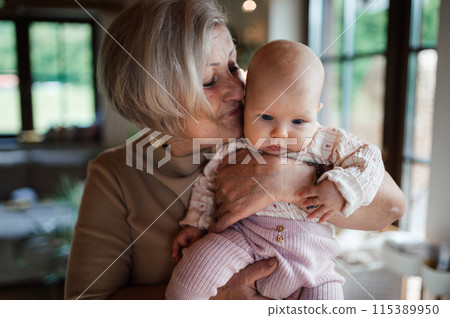Lovely grandmother holding little baby in arms, looking at her lovingly. Strong bond between grandparent and grandchild. Lovely grandmother holding little baby in arms, looking at her lovingly. Strong bond between grandparent and grandchild. 115389950