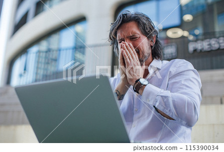 Portrait of mature businessman working on laptop outdoor, recieving bad news. Handsome man with glasses in suit. 115390034