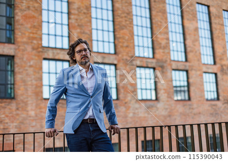 Portrait of mature businessman standing on city street, in front of office building. Handsome man with glasses in suit. 115390043