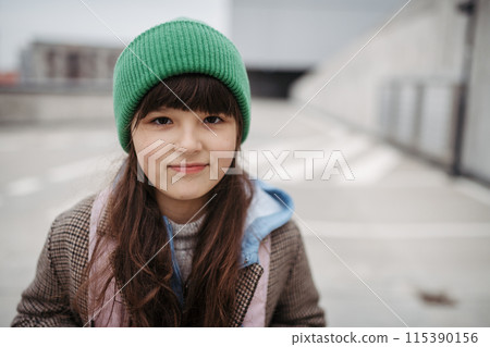 Outdoor portrait of cute young girl with beanie hat. Girl with long hair standing on playground in the city. Outdoor portrait of cute young girl with beanie hat. Girl with long hair standing on playground in the city. 115390156