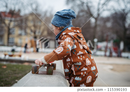 Cute toddler girl playing outdoor in playground with skateboard. Girl in softshell bodysuit spending time in park. 115390193
