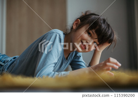 Cute girl lying on belly, scrolling on smartphone. Using social media. Side view. 115390200