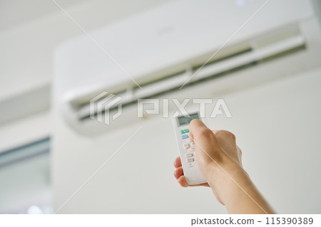 Adjusting air conditioner temperature with remote control. Hand holds remote control and setting comfortable temperature on climate system in apartment 115390389