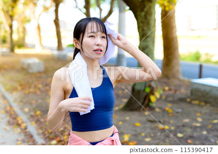 一位年輕女子在秋季公園的樹叢中慢跑,節食,化妝,手裡拿著毛巾。 一位年輕女子在秋季公園的樹叢中慢跑,節食,化妝,手裡拿著毛巾。 115390417