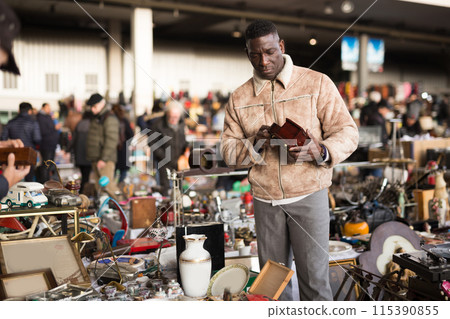 Ordinary Afro-American guy considers things sacond hands on flea market Ordinary Afro-American guy considers things sacond hands on flea market 115390855