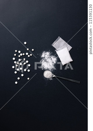 a pile of pills and a spoonful of drug powder against a black background 115391130