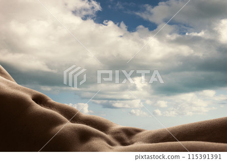 Soft, rolling contours of human body, male muscular torso against vivid backdrop of clouds. Natural forms in human and sky landscape. Soft, rolling contours of human body, male muscular torso against vivid backdrop of clouds. Natural forms in human and sky landscape. 115391391