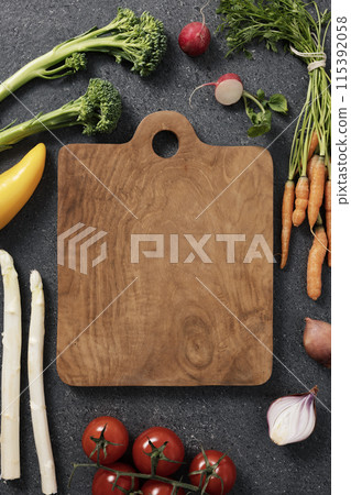 the arrangement of fresh vegetables surrounding a wooden cutting board 115392058