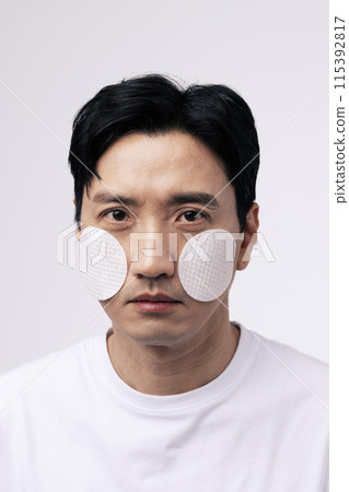 Close up of a middle aged man with a circular cotton pad on both cheeks Close up of a middle aged man with a circular cotton pad on both cheeks 115392817