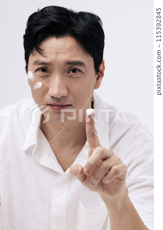 a middle aged man applying cream with his fingers and staring straight ahead a middle aged man applying cream with his fingers and staring straight ahead 115392845