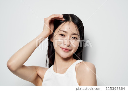 Asian woman posing with her hand on her head against a white background Asian woman posing with her hand on her head against a white background 115392864