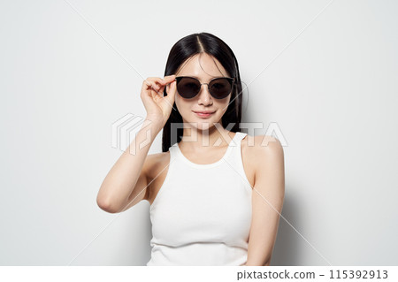 an Asian woman who wears sunglasses with one hand against a white background 115392913
