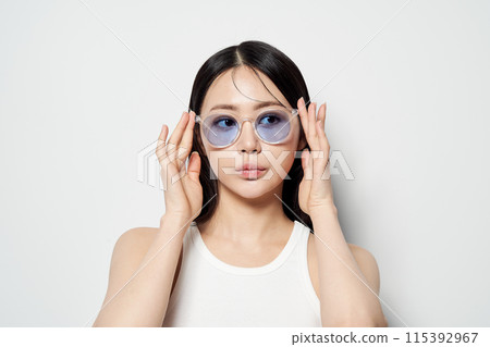 Asian woman staring in one spot wearing transparent sunglasses with both hands 115392967