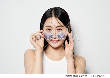 Asian woman staring straight ahead with transparent sunglasses down with both hands 115392968