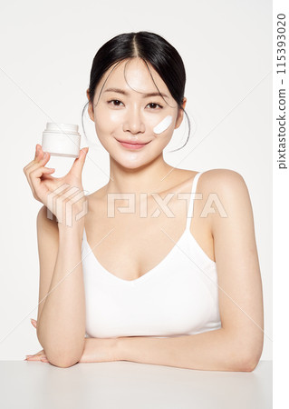 an Asian woman with cream on her face and holding cosmetics an Asian woman with cream on her face and holding cosmetics 115393020