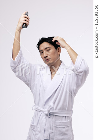 a middle aged man holding a spray bottle and spraying mist on his head 115393350