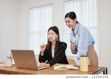 Two women looking at their laptops with bright faces in front of their office desks Two women looking at their laptops with bright faces in front of their office desks 115393745