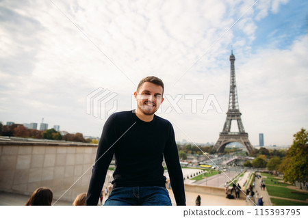 Cheerful man in dark blue pullover is standing on the background of the Eiffel Tower. Cheerful man in dark blue pullover is standing on the background of the Eiffel Tower. 115393795