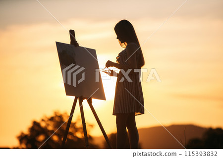 Silhouette of blonde girl paints a painting on the canvas.Palette with paints and spatula, summer sunny day Silhouette of blonde girl paints a painting on the canvas.Palette with paints and spatula, summer sunny day 115393832