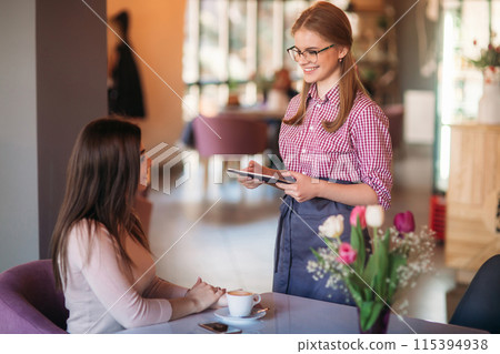 Attractive young waitress using a tablet computer to take an order from a customer in a coffee shop Attractive young waitress using a tablet computer to take an order from a customer in a coffee shop 115394938