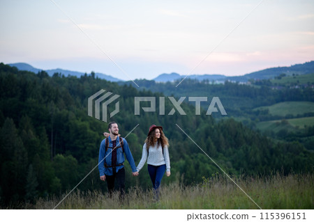Travellers couple hiking on trail in nature with backpacks, during sunset. Young tourist spending summer vacation oudoors, holding hands. Travellers couple hiking on trail in nature with backpacks, during sunset. Young tourist spending summer vacation oudoors, holding hands. 115396151