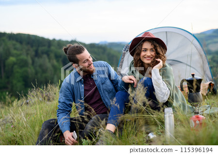 Travellers couple spending time outdoor, sleeping in tent shelter. Young tourist sitting in nature, resting, enjoying sunset. Summer vacation in nature. 115396194