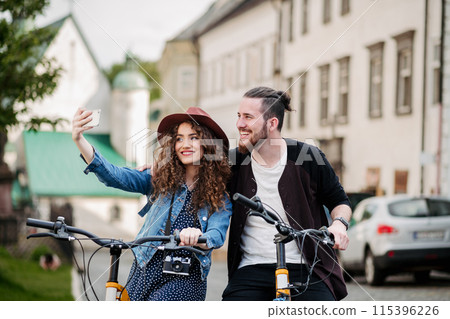 Travellers couple on electric scooters in small city, sightseeing. Young tourist using bikes during their summer trip, vacation. 115396226