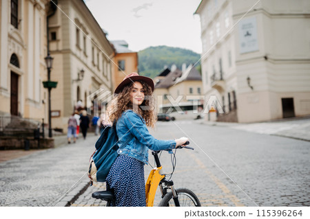 Female traveller on electric scooter in small city, sightseeing. Young tourist using bike during her summer solo trip, vacation. 115396264