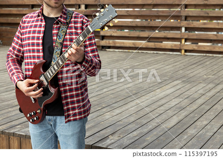 Stylish young guy playing guitar sitting on wooden stage 115397195