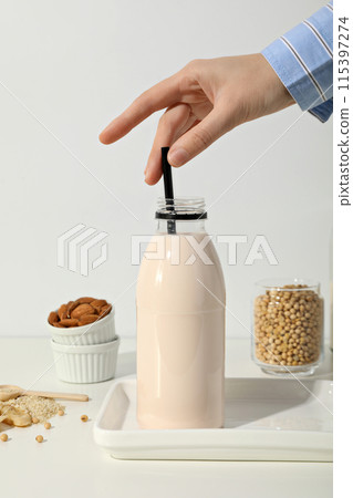 Bottle with milk, hand, nuts in bowl and soy in glass on white background 115397274