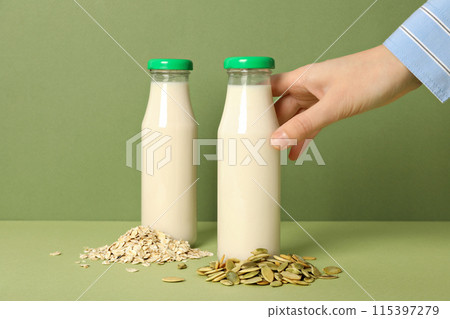 Bottles of milk, hand, oatmeal and pumpkin seeds on green background Bottles of milk, hand, oatmeal and pumpkin seeds on green background 115397279