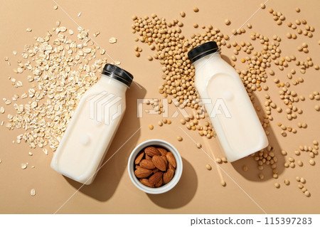 Bottles of milk, nuts in bowl, oatmeal and soy beans on beige background, top view Bottles of milk, nuts in bowl, oatmeal and soy beans on beige background, top view 115397283