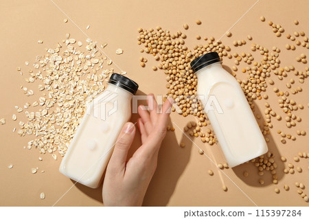 Bottles of milk, hand, oatmeal and soy beans on beige background, top view 115397284
